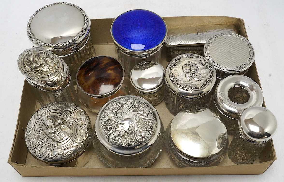 A collection of thirteen assorted late Victorian and later silver topped toilet jars, including blue enamel, tortoiseshell and repousse silver, tallest 9.9cm. Condition - poor to fair to good